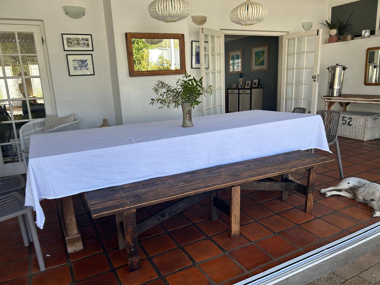 Dining area with a long wooden table covered by a white tablecloth, surrounded by chairs, a rustic bench, and decor.