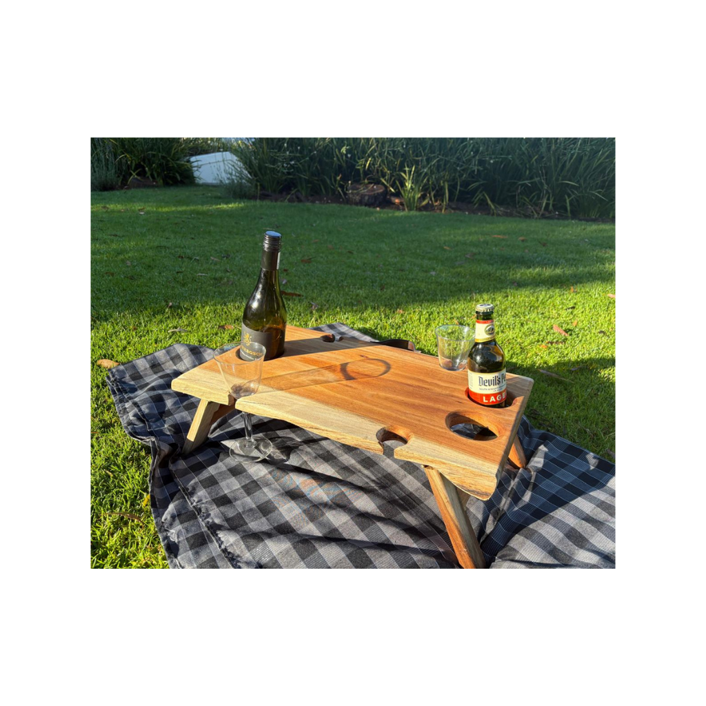Wooden tray with bottles and glasses on a checkered blanket outdoors