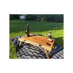 Wooden tray with bottles and glasses on a checkered blanket outdoors