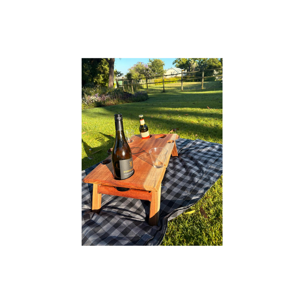Wooden wine table with bottles and glasses on a checkered blanket in a park